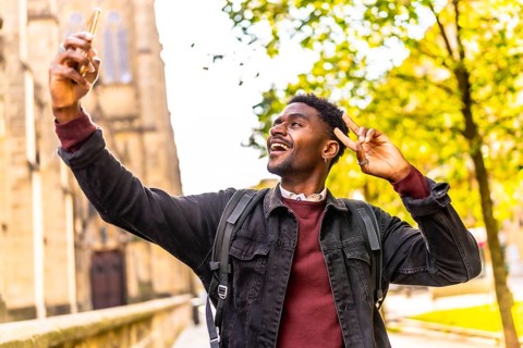 Cool african man taking selfie gesturing success walking at street exploring a city under the