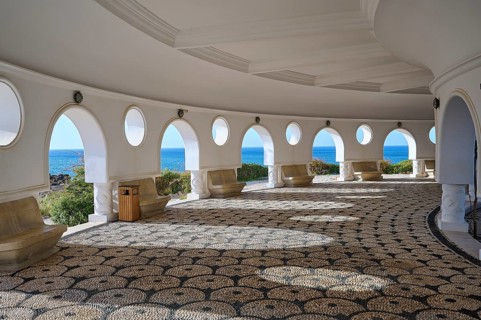 Light-flooded interior of a circular building with round windows offering a view of the sea,