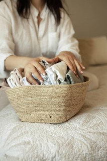 A pregnant woman gently folds baby clothes in a woven basket, preparing for the arrival of her baby