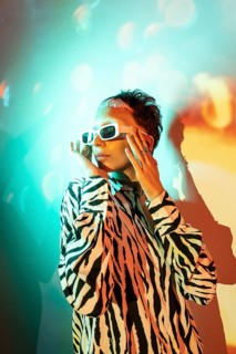 A young, trendy woman wearing a zebra print shirt and fashionable white sunglasses poses