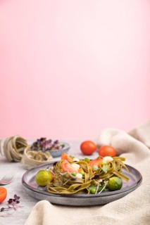 Tagliatelle green spinach pasta with tomato, pea and microgreen sprouts on a gray and pink