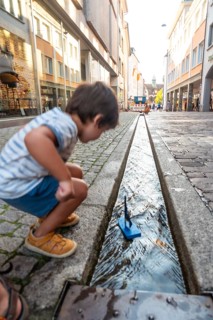 Boy playing with boat on Freiburg im Breisgau canal in summer, Germany