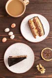 Chocolate biscuit cake with caramel cream, cup of coffee on brown wooden background. top view, flat