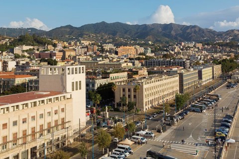High angle view of parking lot with parked sightseeing and tour buses and Messina city skyline,
