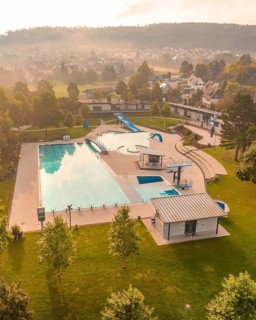 A large swimming pool with surrounding green areas, trees, several buildings, in the morning with