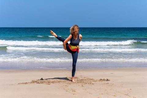 A woman doing yoga on a sandy beach by the sea. Svarga Dvijasana or bird of paradise. Treen Cove,