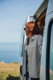 A woman enjoys her remote work lifestyle from a cozy camper van, parked with a scenic ocean view.