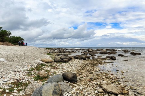 Characteristic coastline, wild natural beach, boulders, hikers on the horizon, dramatic cloudy sky,