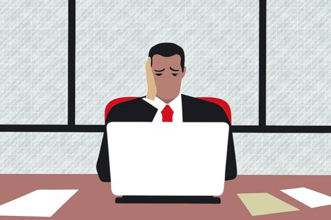 A business professional at a desk shows signs of stress and depression while working on a laptop.