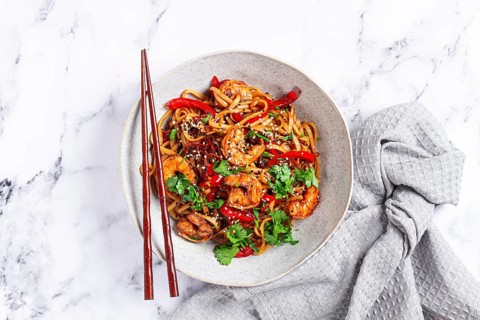 Udon noodles, shrimp with vegetables and fresh herbs, in a bowl with chopsticks, light background,