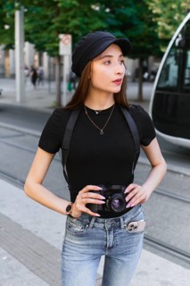 A woman photographer with long hair and casual attire stands in a bustling city street, holding a