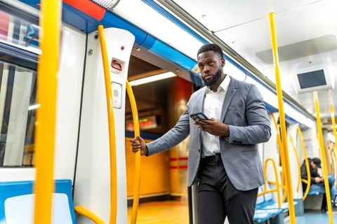Young businessman using mobile phone while commuting on a subway train, holding the handrail and