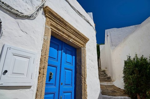 Narrow path with blue wooden door and white walls under a clear blue sky, Chora, main town Patmos,