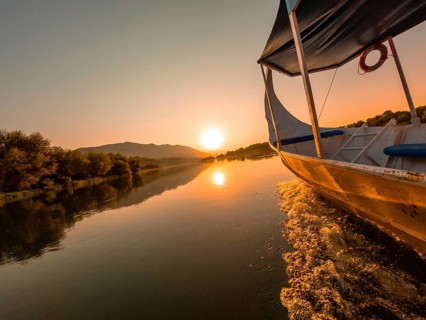 Orange sunset sailing across the lake in a traditional boat on a sightseeing excursion from Shkoder
