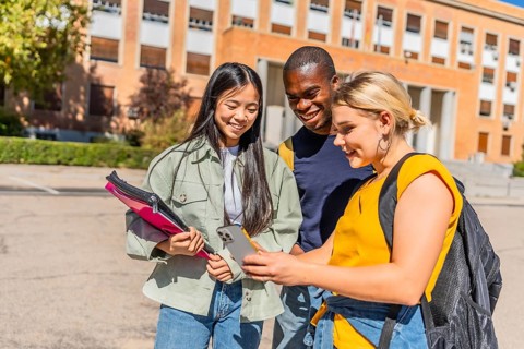 Three multi-ethnic students looking at the mobile phone together standing in the campus
