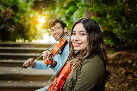 Portrait of two young violists sitting outside. Man and woman violinist sitting on the stairs. Two