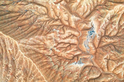 An aerial view showcases a rugged desert landscape marked by intricate erosion patterns The arid