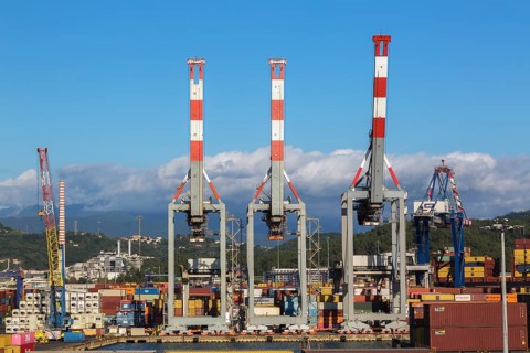 Tall red, white and grey gantry cranes and stacked rectangular metal box shipping containers on