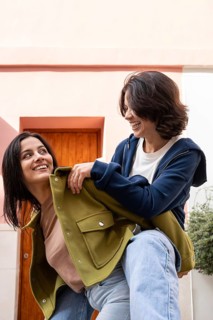 Two women enjoying a playful, joyful moment outdoors. They are dressed casually, smiling at each