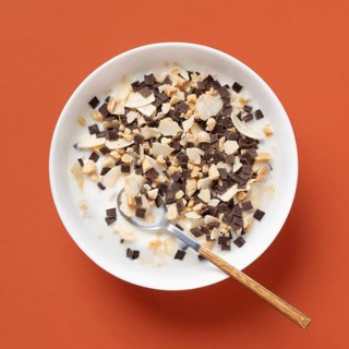 Top view of a white bowl filled with cereal, sliced almonds, and chunks of chocolate, all soaked in