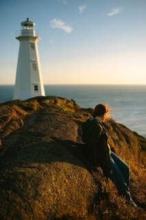 Side view of an unrecognizable woman sitting on rocks, overlooking the ocean near the Cape Spear