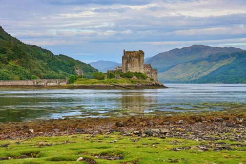 Historic castle in a picturesque river landscape with lush greenery and cloudy skies, Eilean Donan