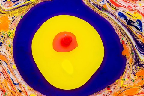 A vibrant paint swirls in bold blues and yellows, centered by a red dot, resembling a modern,