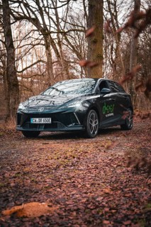 Black limousine with lettering on a forest path surrounded by trees, e-car sharing vehicle from