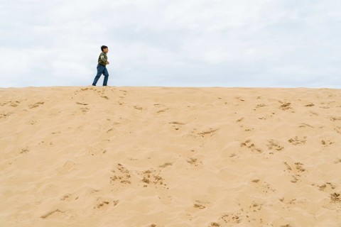 A young boy walks across the dune of Pilat under a cloudy sky in France. The minimal landscape