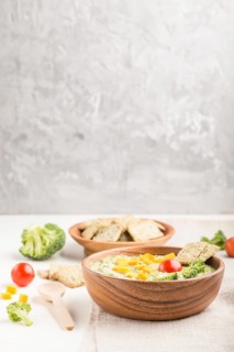 Green broccoli cream soup with crackers and cheese in wooden bowl on a white and gray background