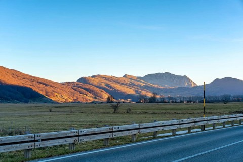 A serene mountain road in the Lazio region of Italy during sunset. The scene features golden-lit