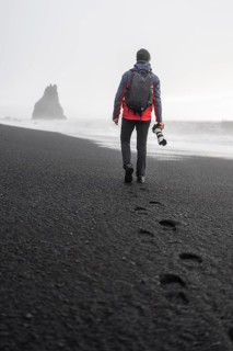 Back view of an unrecognizable photographer with a backpack and camera strolls along the misty