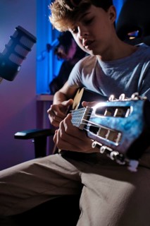 A young musician is captured playing an acoustic guitar while seated in a home recording studio.