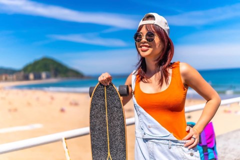 Three quarter length portrait of a chinese cool young woman with skateboard smiling standing next