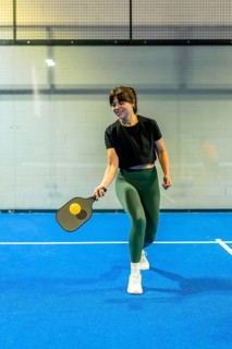 Young athletic woman actively participating in a pickleball game on a vibrant blue indoor court,
