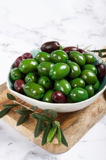 Chalkidiki olives, classic Greek green olives, in a bowl on a cutting board, top view, without