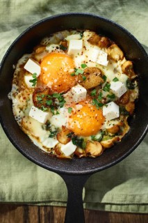 Fried eggs with spinach, mushrooms, grated cheese and feta cheese in small cast iron skillet. Top