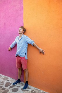 Young man in front of pink and orange house wall with backpack, colourful houses on the island of