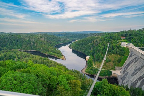 Extensive panorama of a green river landscape with dense forest under a blue sky and clouds,