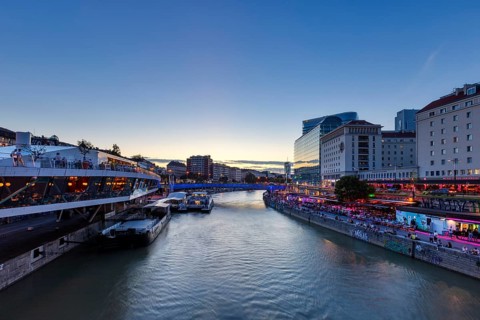 City view at dusk with illuminated buildings along a quiet river, Vienna