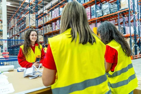 Three females factory workers pack packages for delivery in a distribution warehouse