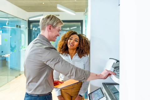 Two businesspeople using a modern multifunction printer in a coworking office, discussing about