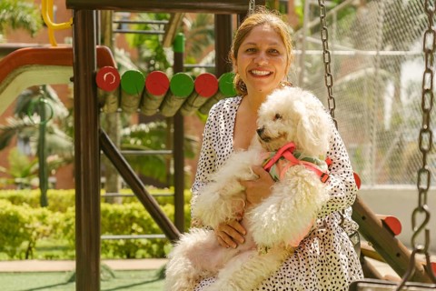 Smiling woman holding her small white poodle dog while sitting and relaxing on a swing at a