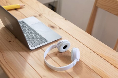 A minimalist workspace with a sleek laptop and white headphones on a light wooden desk. Ideal for