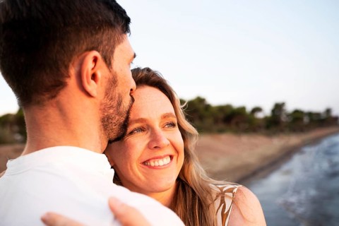 A loving couple embraces on an Italian beach at sunset, their smiles reflecting happiness and