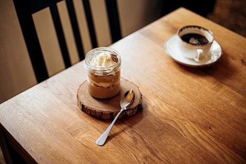 A cozy cafe scene featuring a rustic dessert in a jar on a wooden coaster, accompanied by a