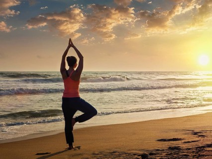 Yoga outdoors, sporty fit woman doing Hatha yoga asana Vrikshasana tre pose on tropical beach on