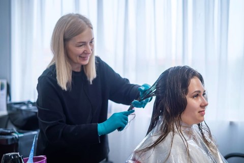 A hair stylist applies keratin treatment to a client's hair in a beauty salon. The stylist wears
