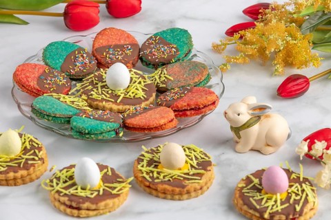 Plate with colourful Easter biscuits, decorated with eggs, next to red tulips