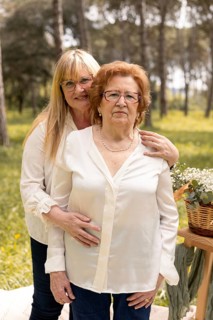 A daughter affectionately embraces her elderly mother in a peaceful outdoor environment, surrounded